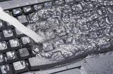 Computer data cleaning concept with fresh water flooding over a black keyboard being poured from the side in a full frame view