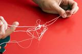 Fixing a problem concept by untangling a knot with a closeup view of hands of a man unravelling a badly knotted piece of string over a red background