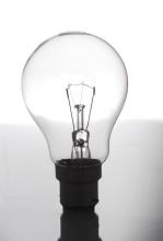 Transparent glass incandescent light bulb balanced upright on a reflective surface in a power and energy concept