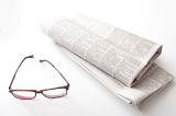 Reading newspapers concept with a pair of glasses and two folded fresh newspapers on white table surface in close-up