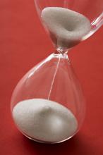 Passing of precious time concept with a close up tilted view of sand running through an hour glass over a red background
