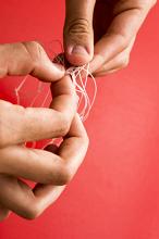 Untangled concept with man unravelling a knot in fine twine with his fingers over a red background with copy space