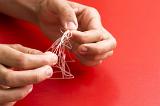 Working on Problem concept with the hands of a man untangling a knot in fine twine over a red background with copy space