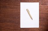 Concept of writers block with blank white page of paper with a ballpoint pen on top lying on a desk viewed from above