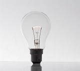 conceptual image of a glowing lightbulb stood alone on a light background and reflective surface