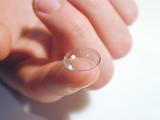 Close Up of Person Holding Contact Lens on Tip of Finger on White Background
