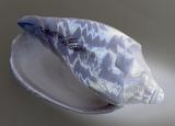Grey and white patterned conch seashell lying diagonally on a grey background, close up detail