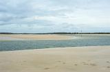 River estuary crossing deserted golden beach sand as it winds its way to the sea under a cloudy sky