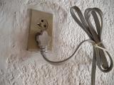 Domestic wall mounted electrical socket with an attached plug and cable supplying household electricity