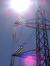 View looking up into the sun of a high voltage electricity pylon with pink sun flare spots