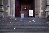 Litter strewn stone steps in front of a public venue with scattered plastic and cardboard drinks cartons, paper and rubbish