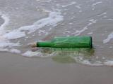 Discarded green glass bottle with a cork left abandoned in shallow surf at the seaside ready to add to global marine pollution