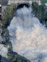 White frothy water gushing from a stormwater culvert with great force into a channel during flooding