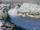 Water gushing from a stormwater drain or culvert with powerful force as it flows into a rock line drainage canal or waterway
