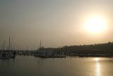 The sun makes a valiant effort to shine through thick hazy smog caused by air pollution over a coastal marina with small boats and pleasure yachts moored at the jetties