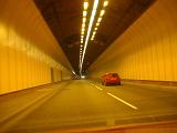 Car driving through a covered illuminated traffic tunnel causing air pollution through exhaust emission in the confined space
