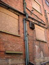 Old metal pipes attached to the exterior brickwork of a building with a rusted airconditioning duct