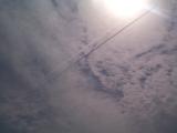 Low Angle Abstract View of Jet Contrails Streaking Across Cloudy Blue Sky Underneath Bright Eclipse Sun