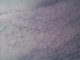 High Angle View of Jet Streaking Contrails Across Sky and Casting Shadow on Blanket of White Puffy Clouds