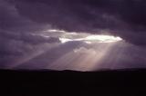 Beautiful and Dramatic Scenic of Inspirational Sunrays Shining Through Heavy Storm Clouds in Vast Sky onto Dark Landscape