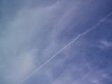 Low Angle View of Jet Contrail Streaking Across Vast Blue Sky with Wispy Clouds