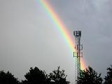 Colorful rainbow of refracted light on water droplets arcing through the sky behind a telecommunications tower on a wet rainy day