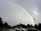 Colorful Rainbow Arching Over Rain Soaked Parking Lot in Cloudy Sky in Aftermath of Rain Storm