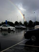 Colorful rainbow on a rainy day viewed across a wet parking lot with cars breaking through stormy grey clouds