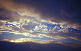 Beautiful and Dramatic Blue Sky Shrouded in Heavy Dark Clouds at Sunrise or Sunset with Golden Sun Disappearing Behind Clouds