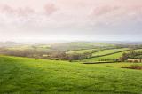 Scenic landscape view of lush rolling green hills in the English countryside with sunlight breaking through morning mist and cloud