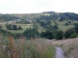Footpath leading cross rolling hills with distant houses on the hilltop and a wooded valley below