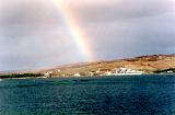 Colorful rainbow in stormy grey cloudy coastal skies above a small fishing village in a bay viewed across the water