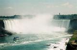 View of Niagara Falls from downstream with a tourist boat approaching the foot of the waterfall and cloud of spray