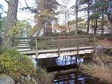 Rustic foot bridge over a stream feeding a country lake in Cumbrian woodland
