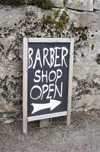 Handwritten sign - barber Shop Open with arrow standing in front of a concrete exterior retaining wall