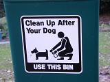 Clean Up After Your Dog black and white sign in park on plastic bin in close-up with dog and owner pictogram