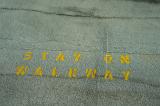 Stencilled street sign - Stay On Walkway - painted in yellow on the asphalt viewed from overhead