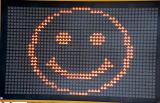 Emoticon of a happy smiling face in orange on an electronic sign in a close up full frame view