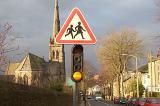 Traffic light below a school warning sign in a town street at dusk with old stone church with tall steeple