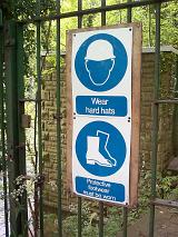 Warning sign to wear protective gear before entering a gate with specific mention of hardhats and footwear