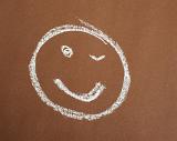 Smiley face with a wink hand drawn in chalk on a brown background