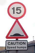 Road sign for speed humps and 15 speed limit viewed in close-up from low angle against grey sky
