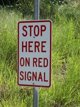 Warning Stop Sign to stop on the red signal against a grassy verge on a road in an oblique angle view