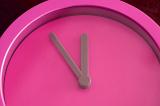 Overhead close up view of bright pink clock with grey hands and no numbers