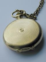 Closed vintage full hunter pocket watch with a tooled and engraved case and chain, closeup high angle view showing the texture of the embossing
