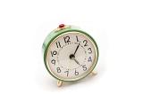 Still Life of Round Green Vintage Wind Up Alarm Clock with Red Snooze Button on Top with White Background, Time Shown is Seven Minutes Past Five