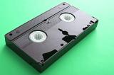 Old unlabelled VHS video cassette tape lying on a green background with copy space in a personal entertainment concept