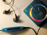 Blue plastic Mini DisÑ Sony personal portable music player with controls on cord and black earbuds on white table surface shot from above