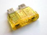Yellow automotive fuse or circuit breaker for use in your car in a close up view on the plastic over white