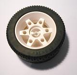 A Toy car tyre with white alloy rim lying on a white background with shadow viewed from above